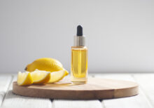 Yellow cosmetic oil and sliced lemon pieces on the light wooden and gray background close-up picture. Natural cosmetics with fruit acid concept